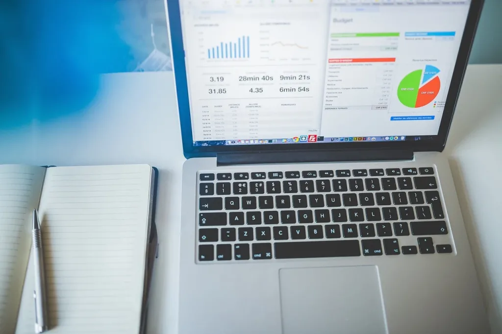 Laptop displaying charts beside an open notebook and pen on a desk