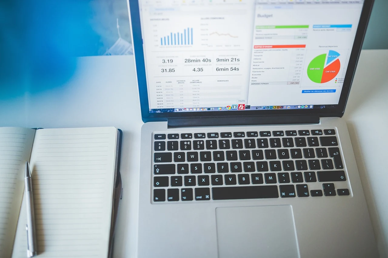Laptop displaying charts beside an open notebook and pen on a desk